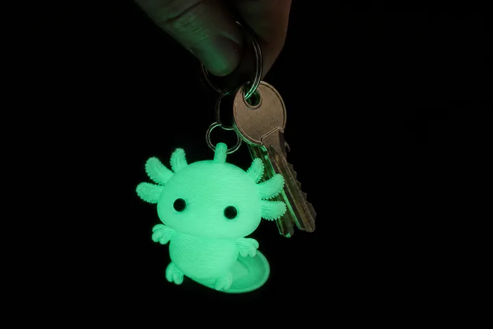 Llavero de ajolote impreso en PLA fosforescente brillando en verde junto a unas llaves